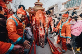 A groom assists his bride as she steps down from a traditional Chinese sedan chair, marking her arrival at his home for their wedding celebration in Kaifeng, China.